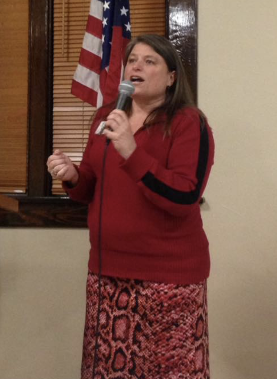 Teresa speaking at a podium with American flag